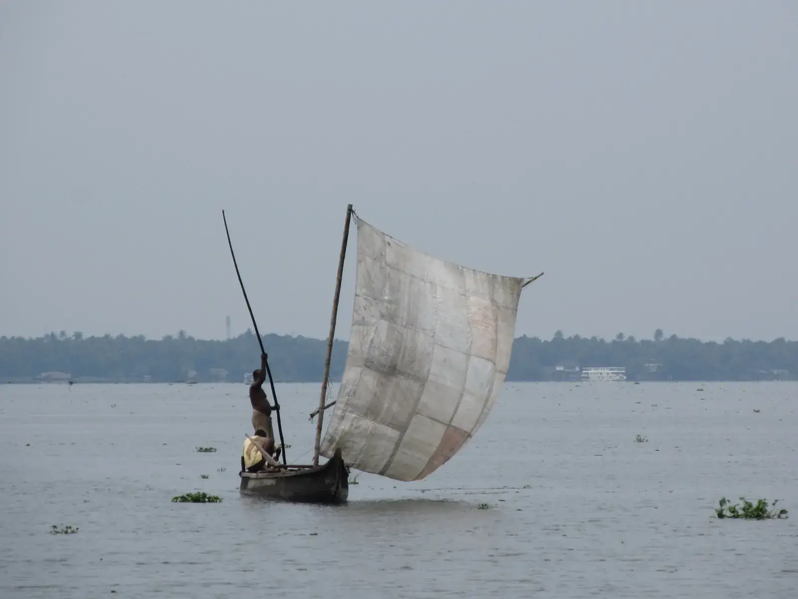 A small boat with a patched sail crossing a wide grey river