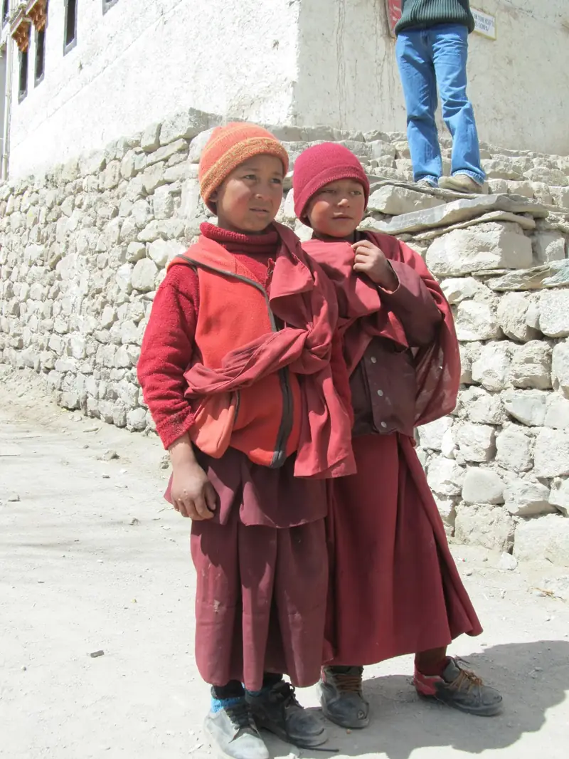 Two young monks in red robes beside a stone wall